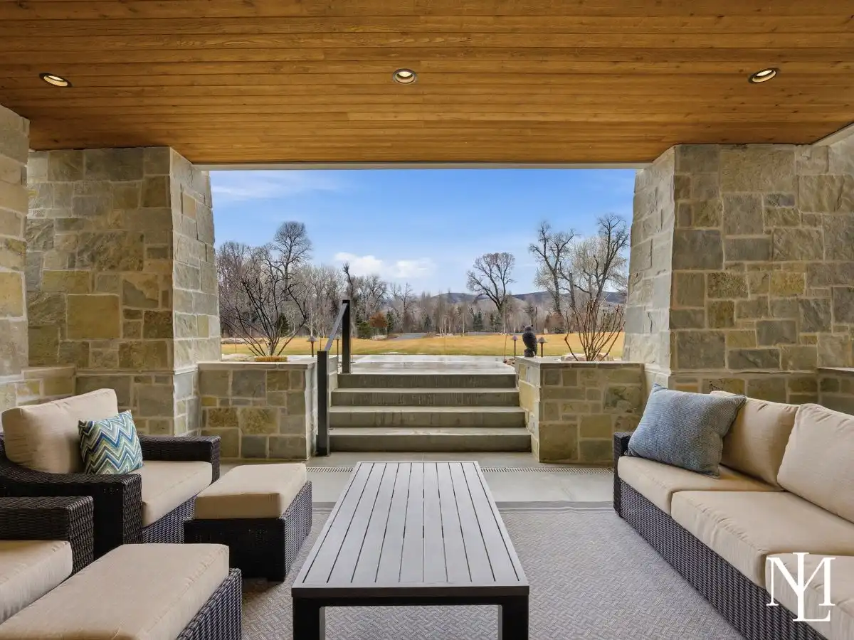 Covered outdoor lounge with stone columns, wood ceiling, and open views across the lawn in luxury Huntsville home.