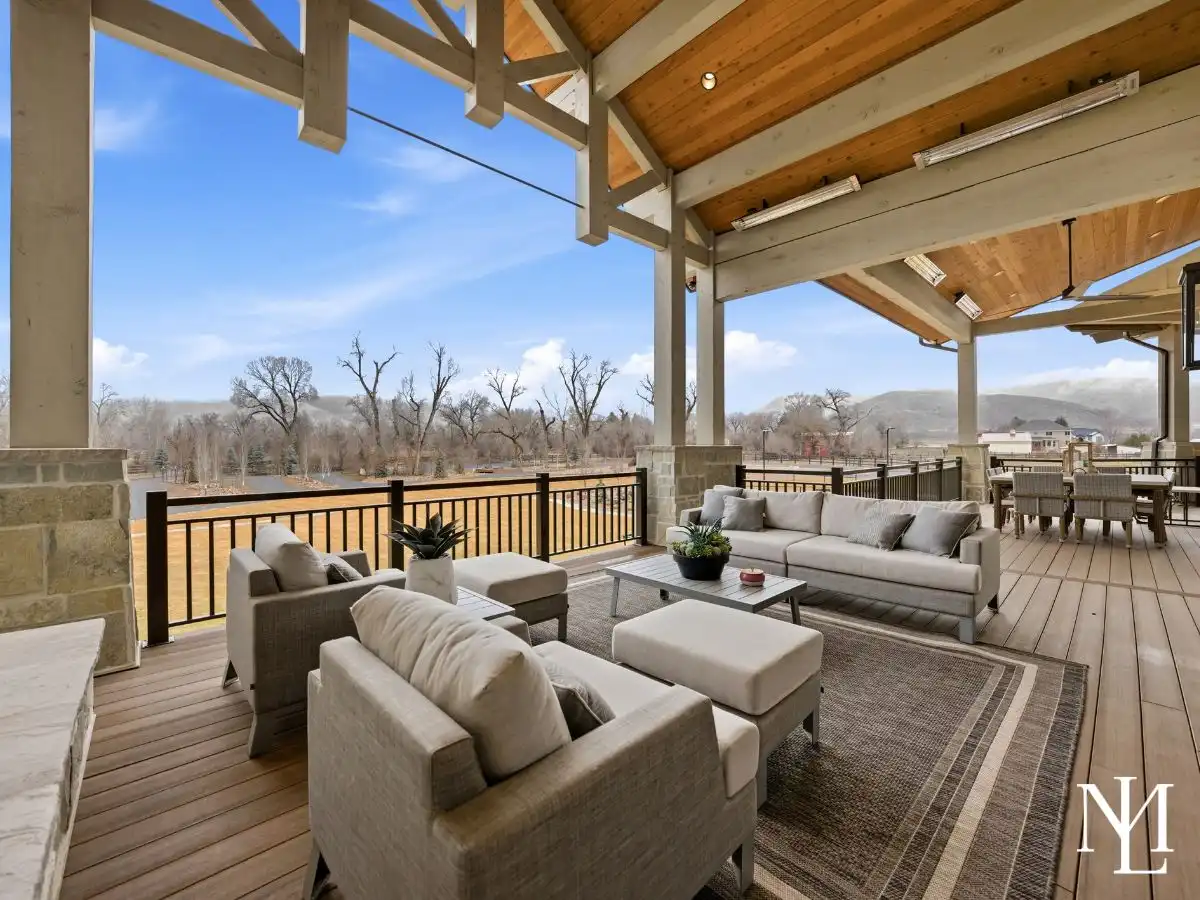 Covered outdoor living deck with lounge seating, timber beams, and views across open space in Huntsville Utah.