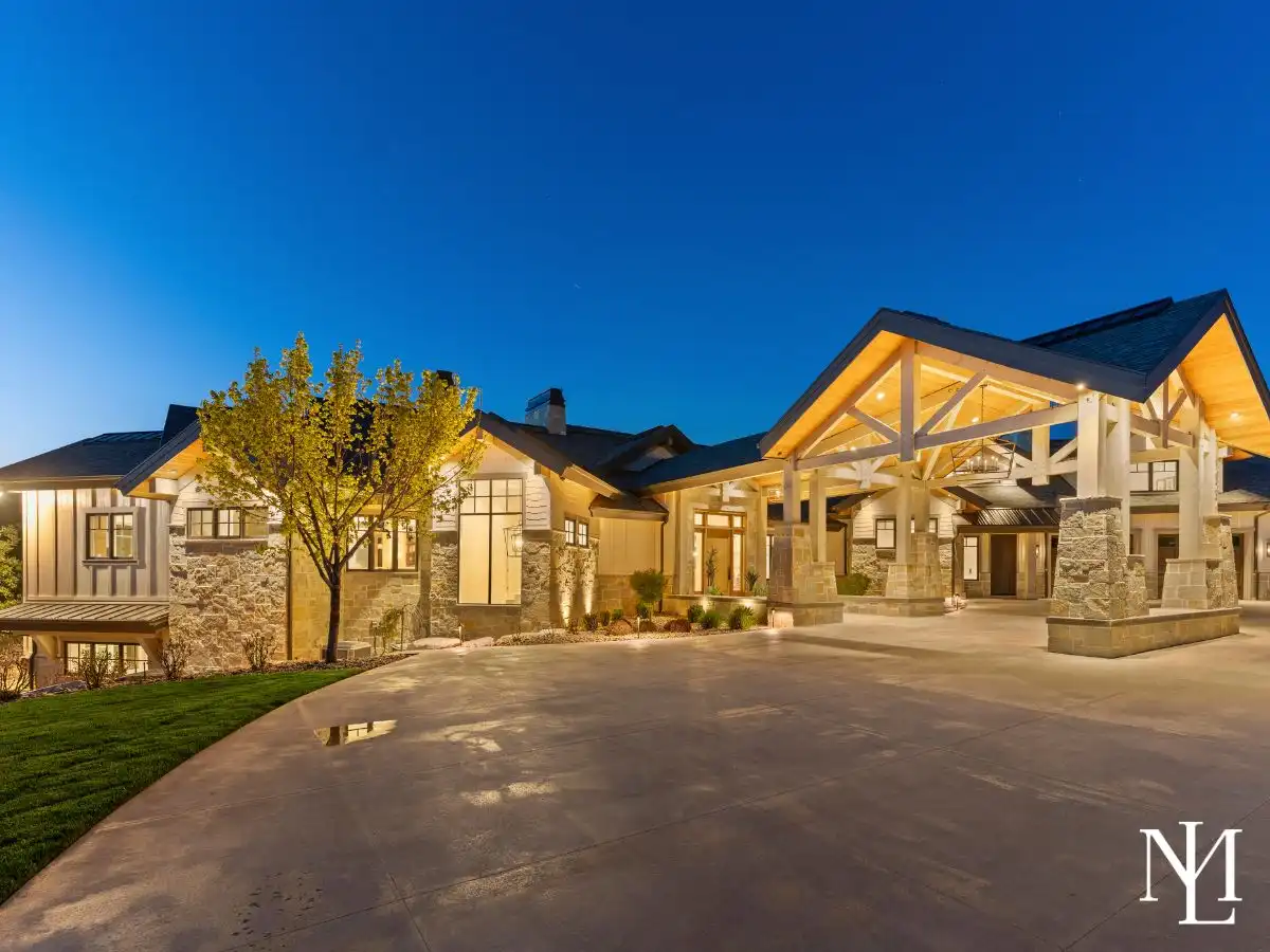 Evening exterior of custom luxury home in Huntsville Utah with illuminated timber entry, stone detailing, and grand covered drive.