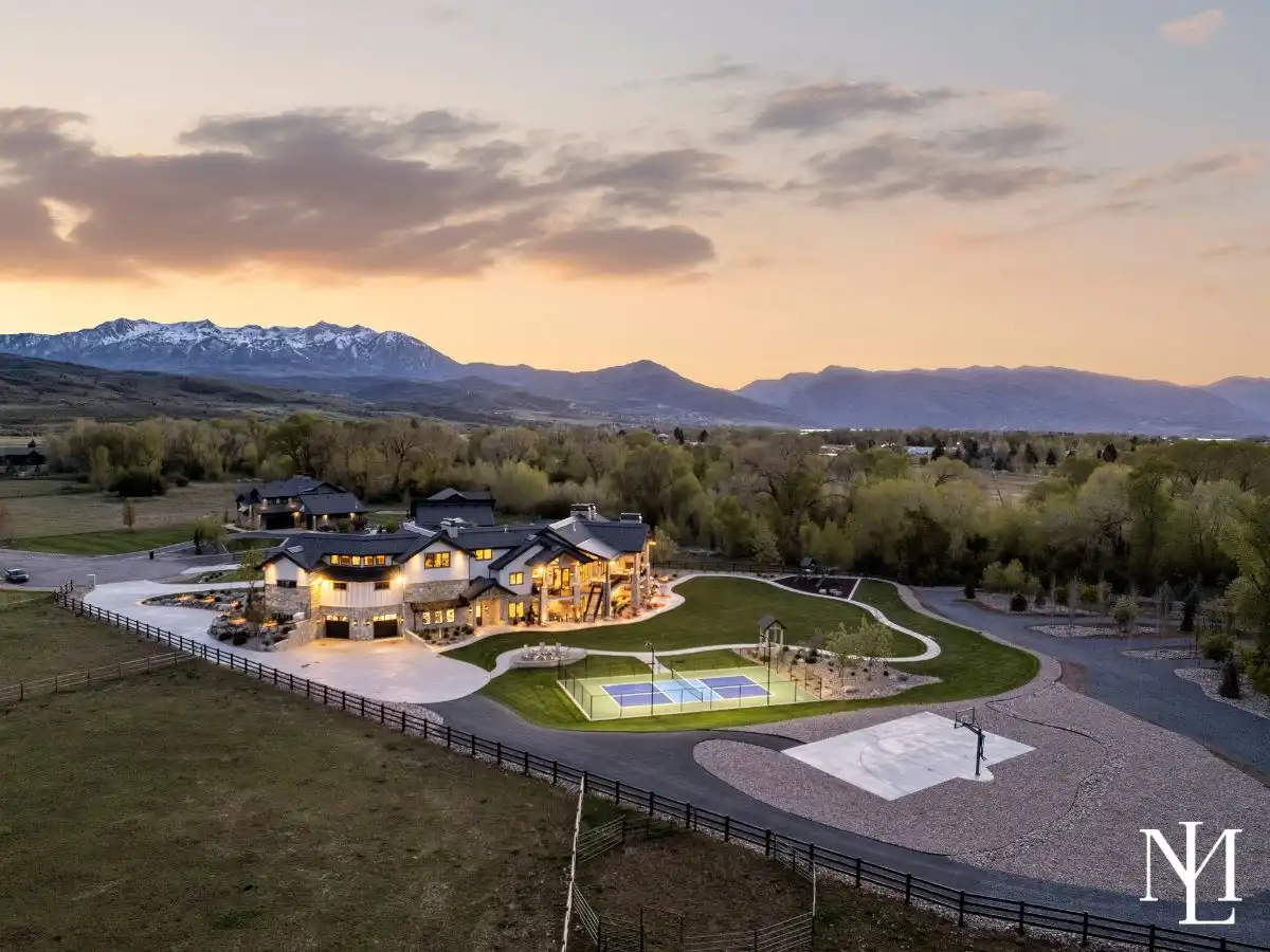 Twilight aerial of luxury Huntsville Utah estate with sport court, basketball court, sweeping grounds, and panoramic mountain views.
