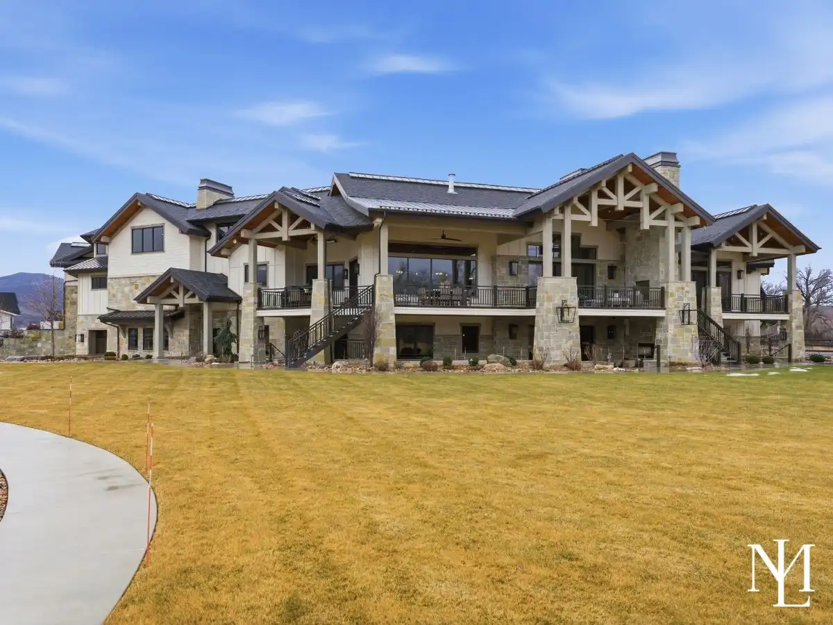 Rear exterior of custom Huntsville Utah estate with expansive lawn, covered decks, timber architecture, and mountain setting.