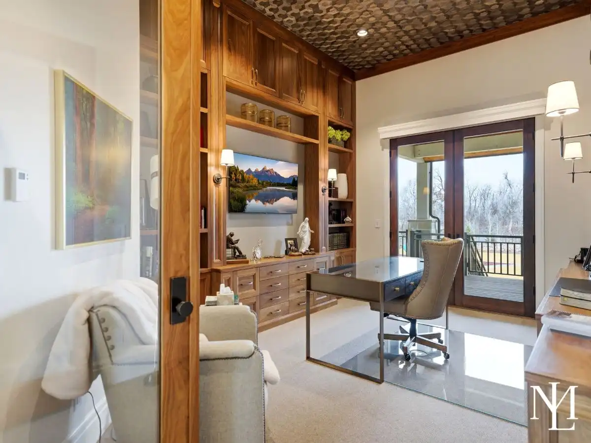 Custom home office with built-in wood cabinetry, French doors, and private covered deck access in luxury Huntsville home.