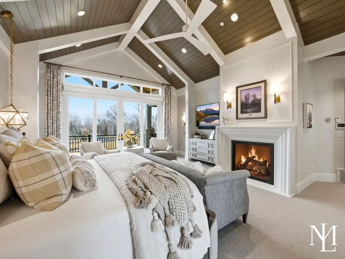 Elegant primary suite with vaulted ceiling, fireplace, large windows, and soft neutral finishes in Ogden Valley luxury estate.