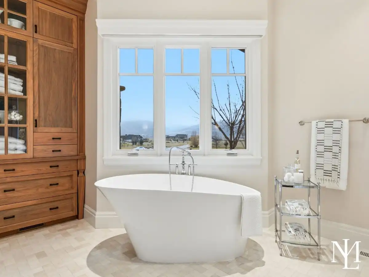 Freestanding soaking tub beneath large picture window in spa-inspired primary bathroom with mountain views.