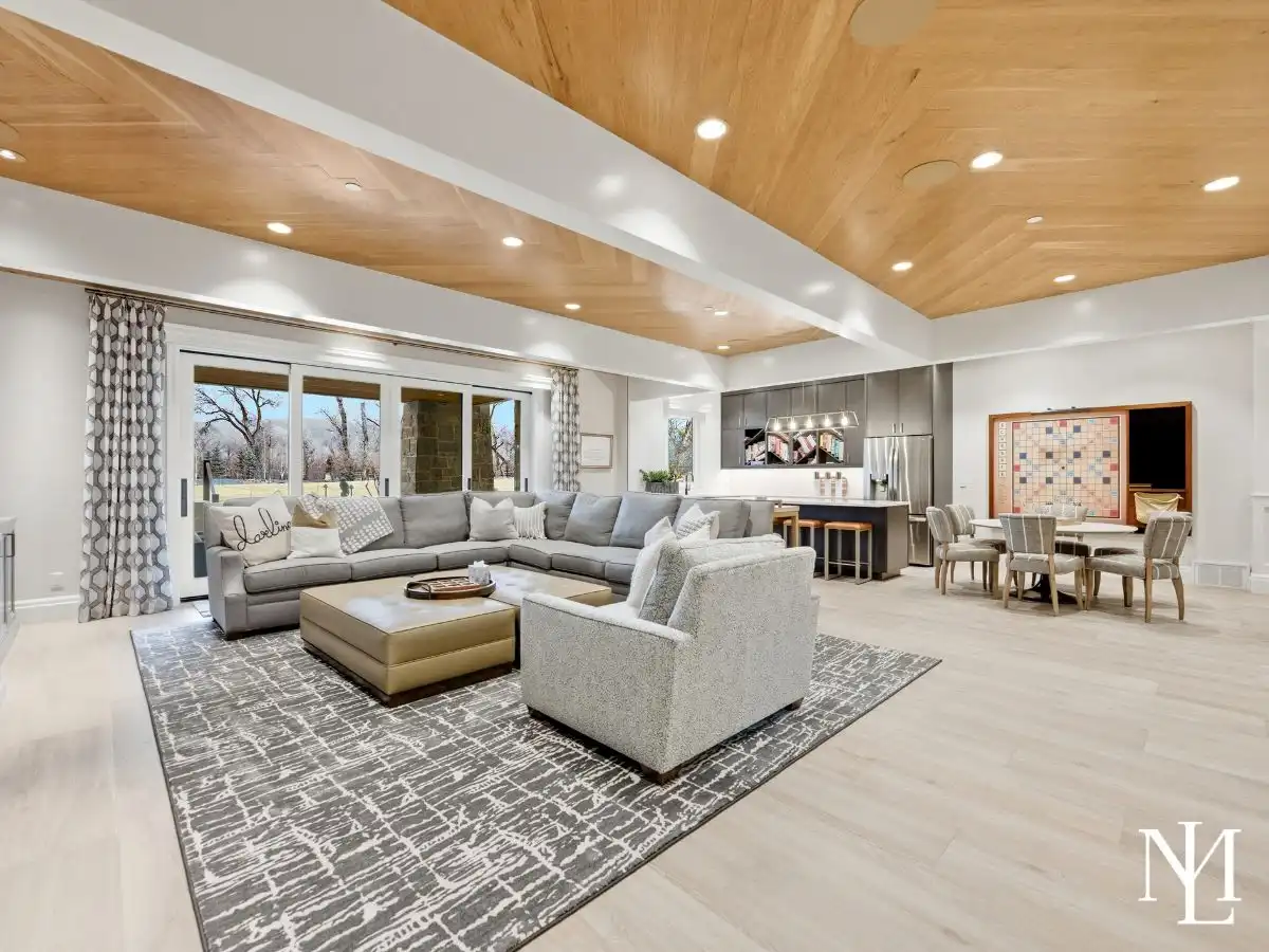 Expansive lower-level family room with sectional seating, game table, kitchenette, and sliding doors to outdoor patio.