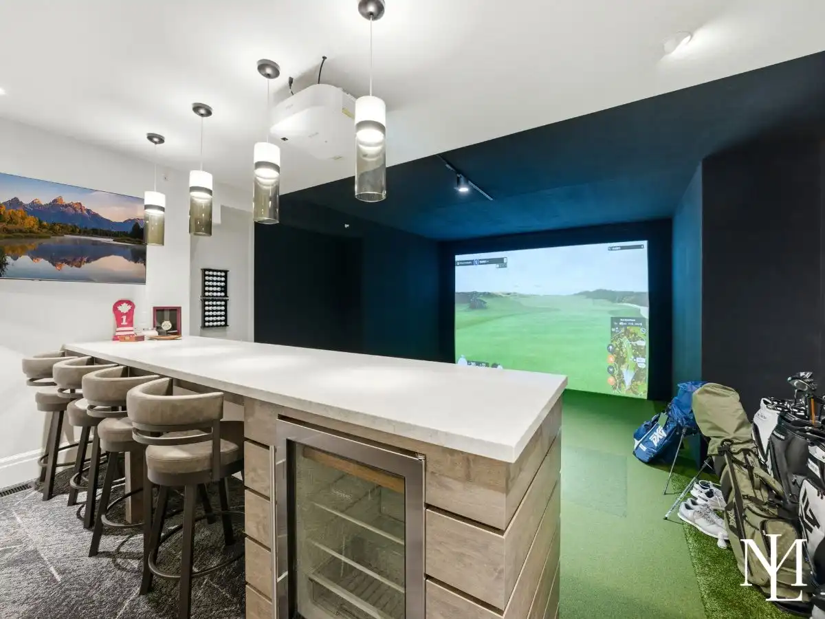 Indoor golf simulator with bar seating, beverage fridge, and entertainment space in custom Ogden Valley estate.