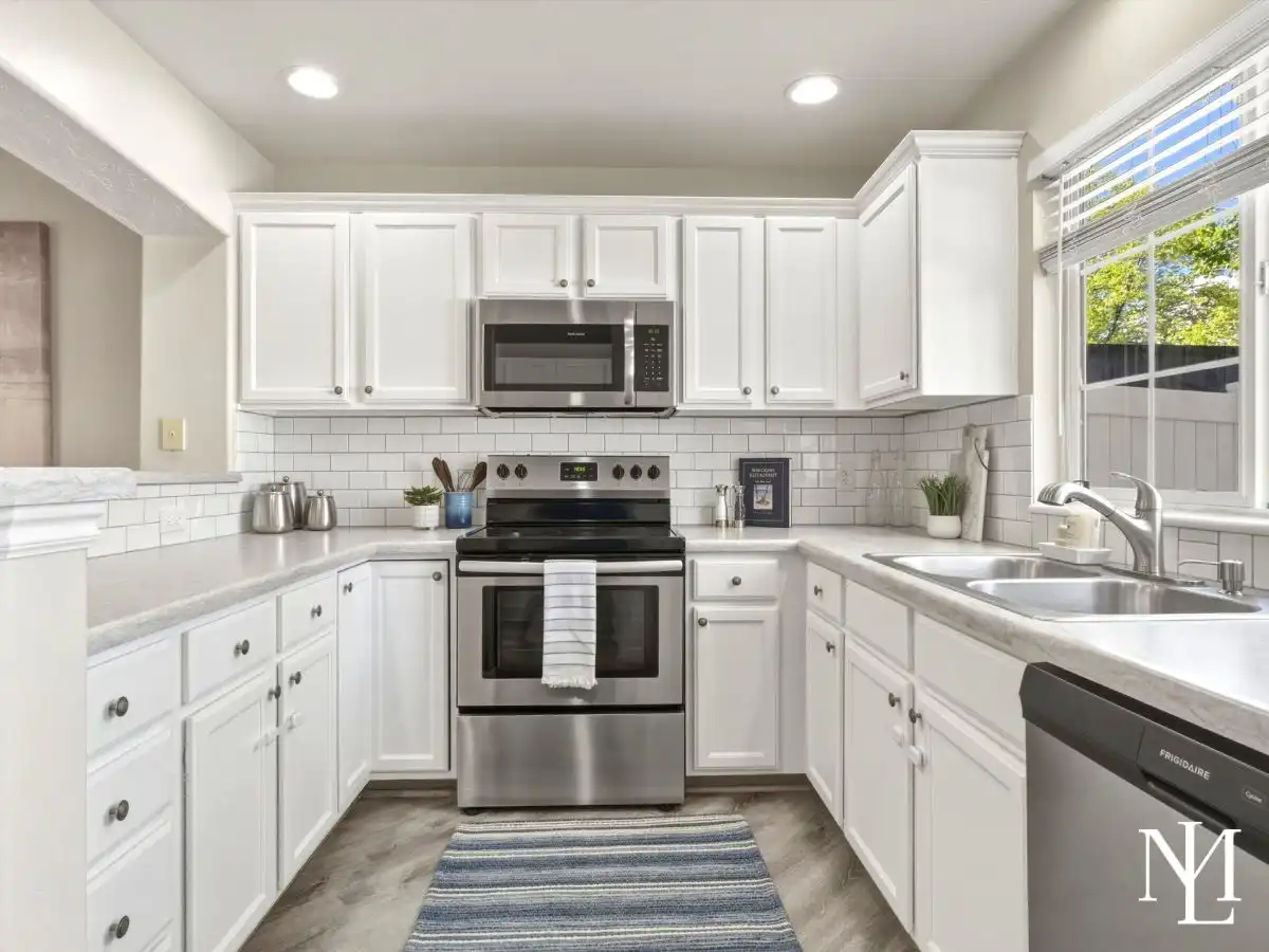 Updated white kitchen in Draper townhome with stainless steel appliances, subway tile backsplash, and window over the sink