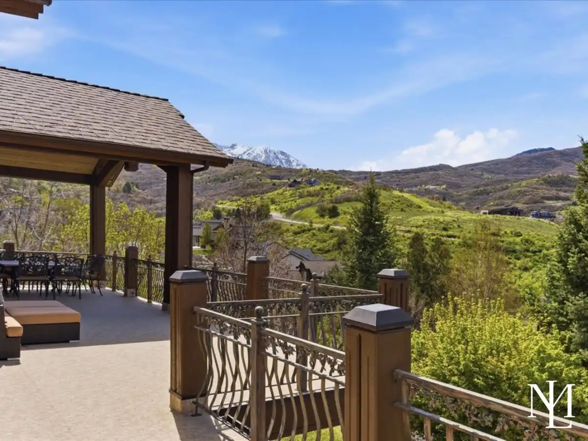 Expansive deck with decorative railing and sweeping mountain views across lush green hills and the surrounding valley.