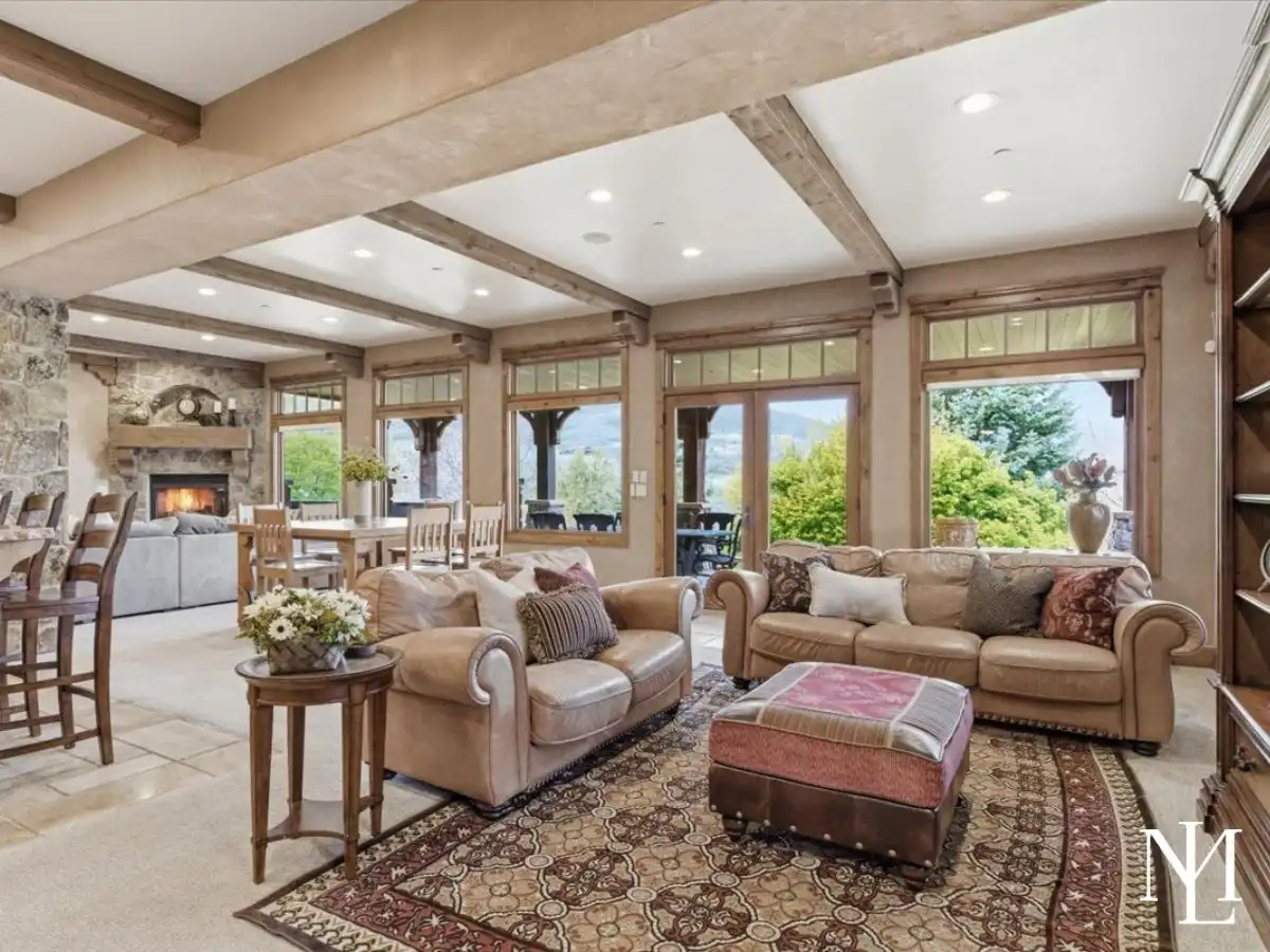 Open gathering room with leather seating, exposed beams, large picture windows, and seamless flow to dining and outdoor living.