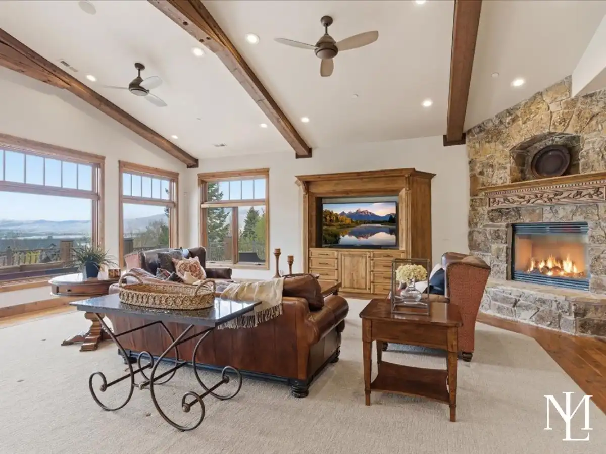 Vaulted great room with exposed beams, stone fireplace, leather seating, and large windows framing mountain and valley views.