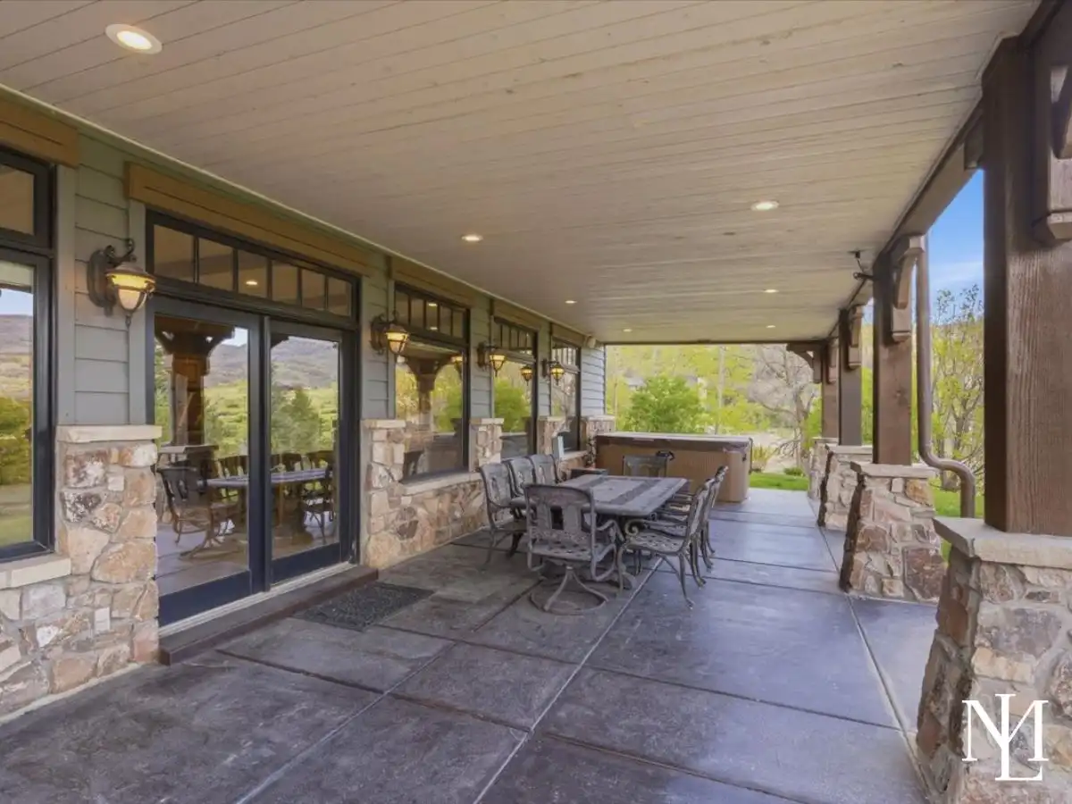 Covered outdoor patio with dining area, hot tub, stone columns, and easy indoor-outdoor living for year-round entertaining.
