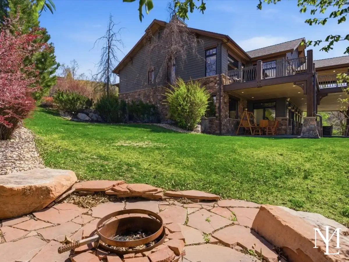 Rear exterior of the home with covered decks, manicured lawn, and layered outdoor living spaces tucked into a mountain setting.