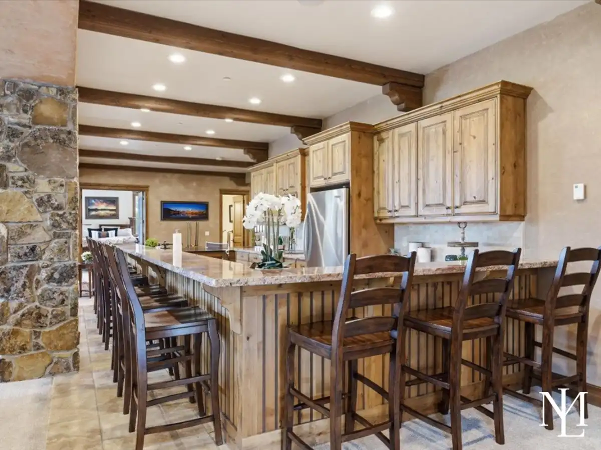 Long entertaining bar with extensive seating, wood cabinetry, stone counters, and open connection to the main living spaces.