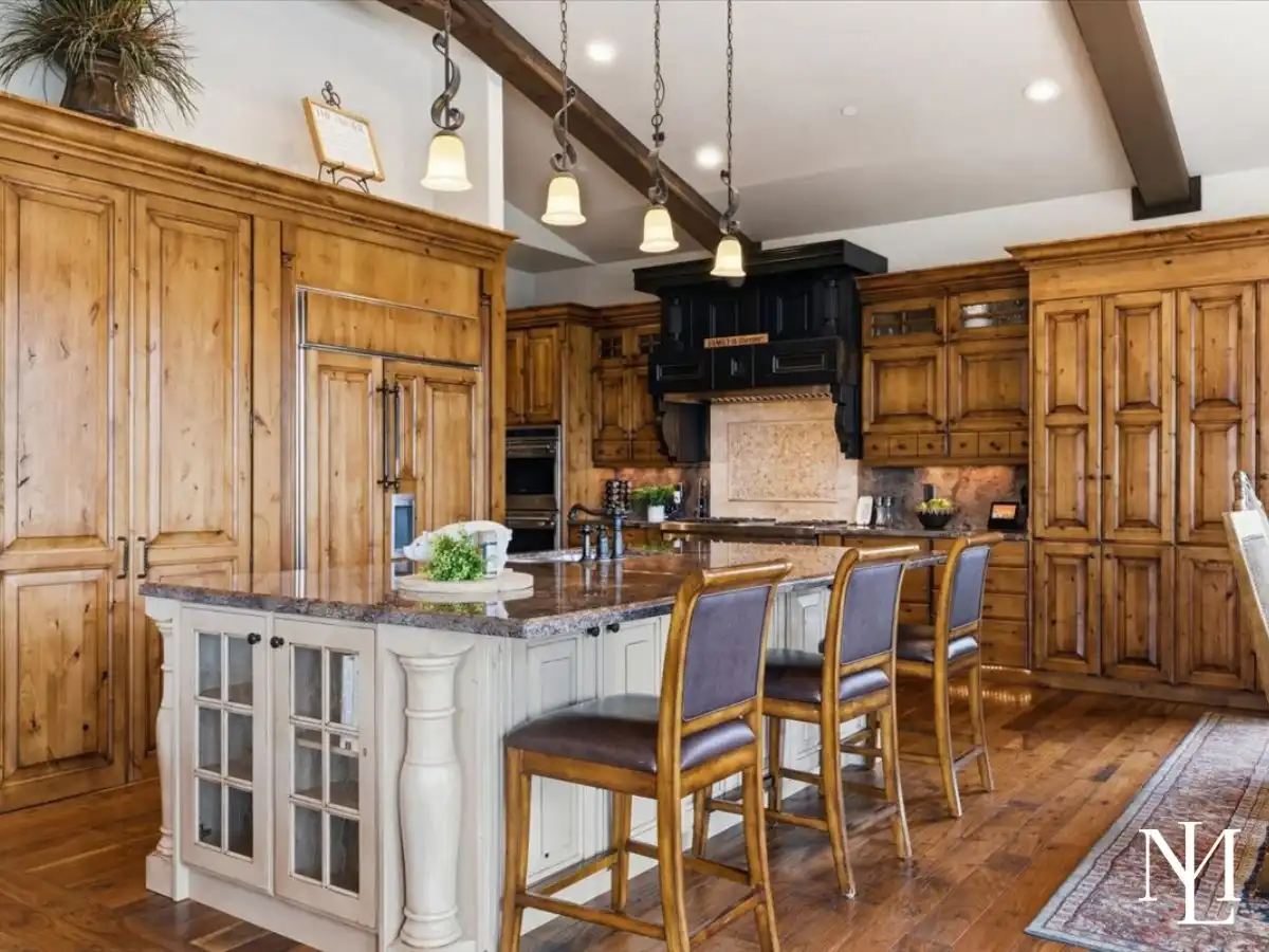Custom kitchen with natural wood cabinetry, oversized island seating, stone countertops, and high-end appliances in a mountain-style interior.