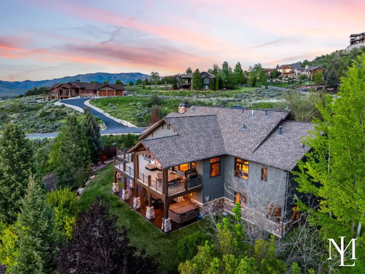 Aerial dusk view of the luxury mountain home with covered decks, landscaped yard, and neighboring custom homes across the hillside.