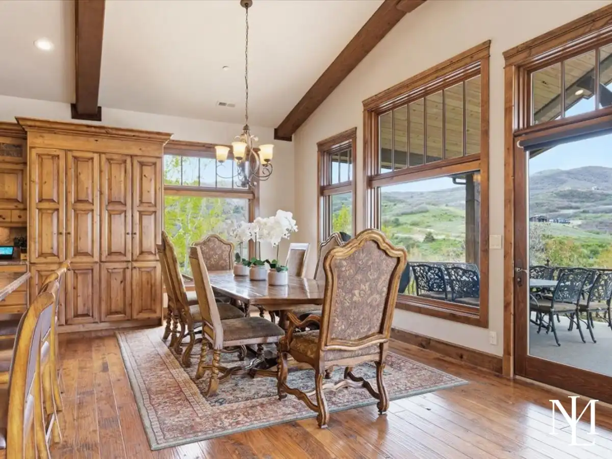 Warm dining area with wood floors, elegant chairs, oversized windows, and direct access to a covered patio with hillside views.