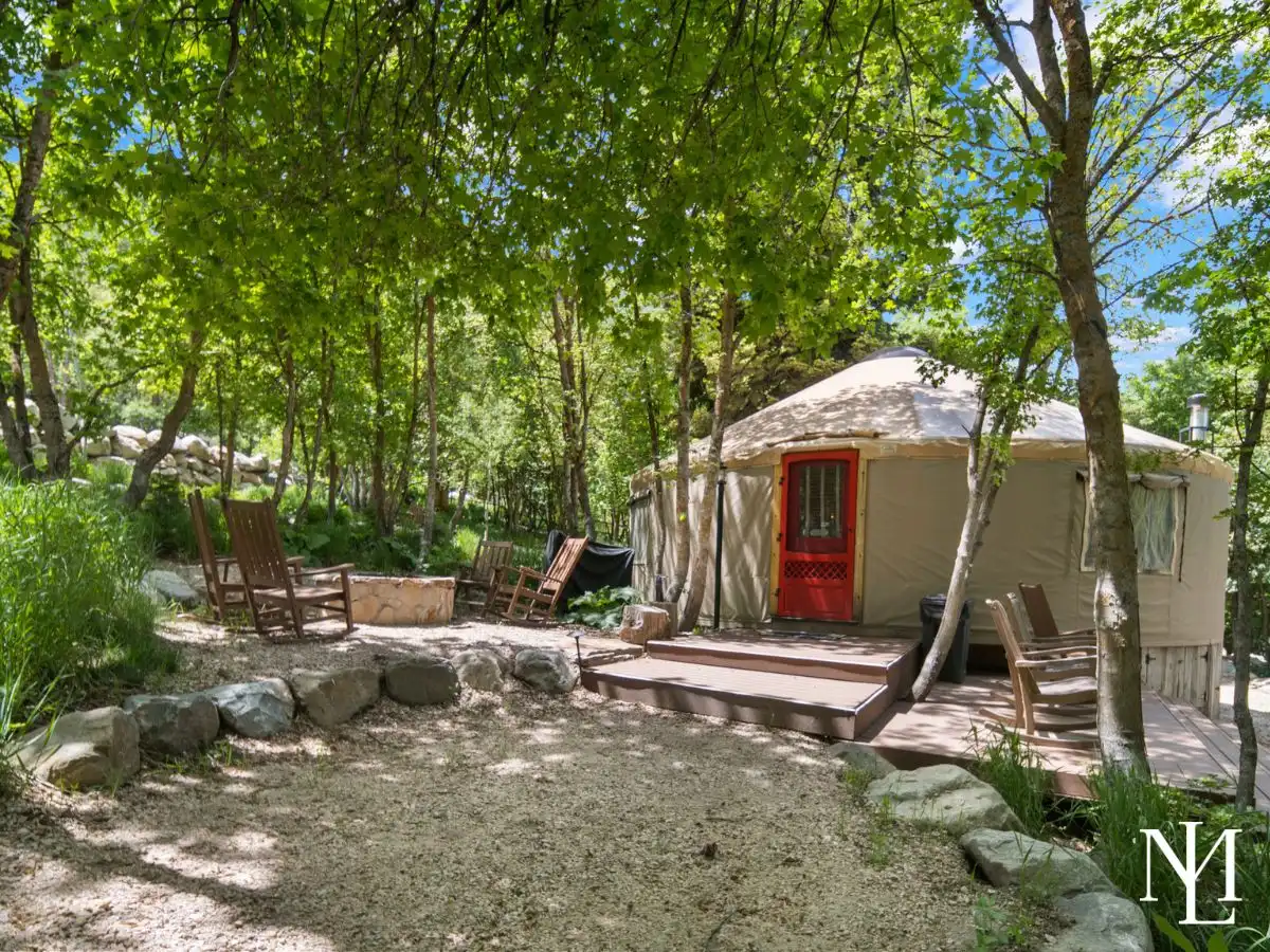 Secluded yurt retreat with red door, outdoor seating, and wooded surroundings in Ogden Valley.