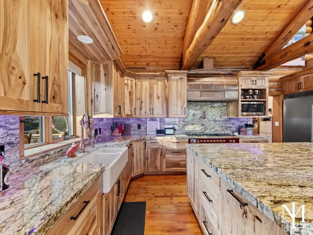 Rustic luxury cabin kitchen with natural wood cabinetry, exposed beams, granite countertops, farmhouse sink, and professional range.