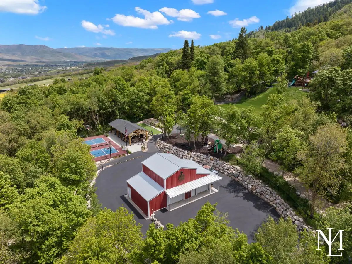 Aerial view of a private mountain estate with a red barn, pickleball court, pavilion, and activity areas in Liberty, Utah.