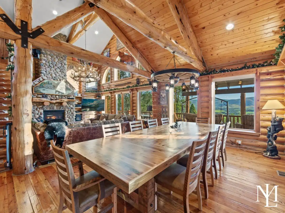 Large log cabin dining room with vaulted wood ceilings, exposed timber beams, stone fireplace, and expansive mountain views.