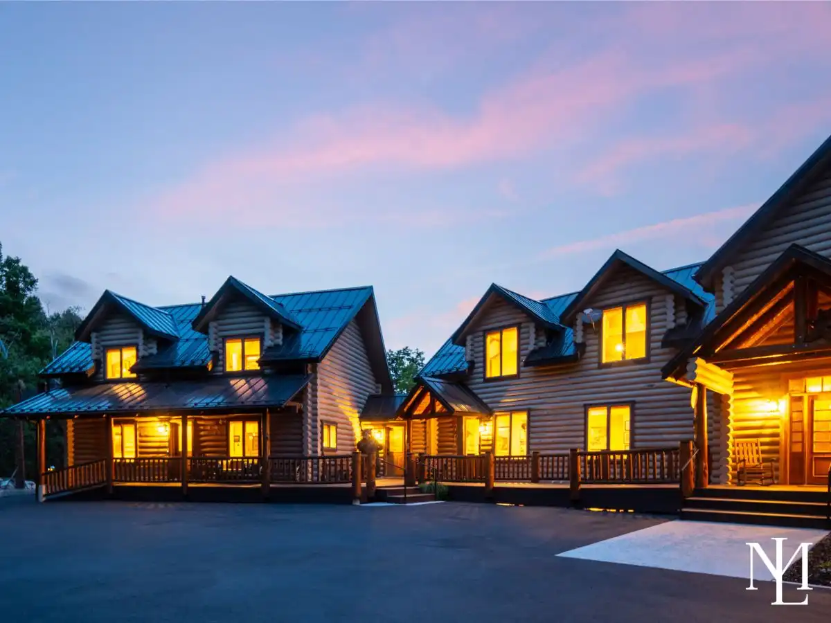Twilight exterior of a luxury log cabin estate in Liberty, Utah, with warm window light, covered porches, and a pink mountain sky.