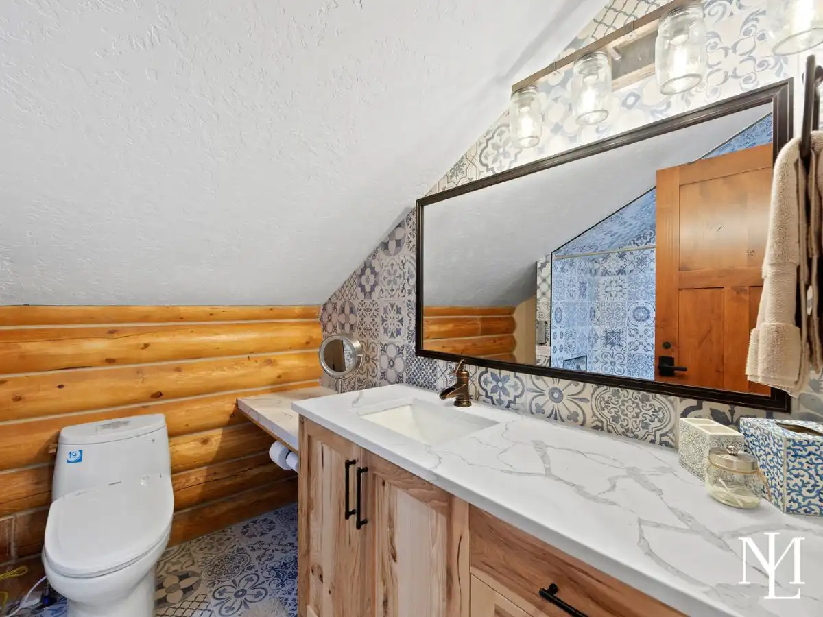 Updated cabin bathroom with patterned blue tile, wood vanity, quartz-style countertop, and log wall accents.