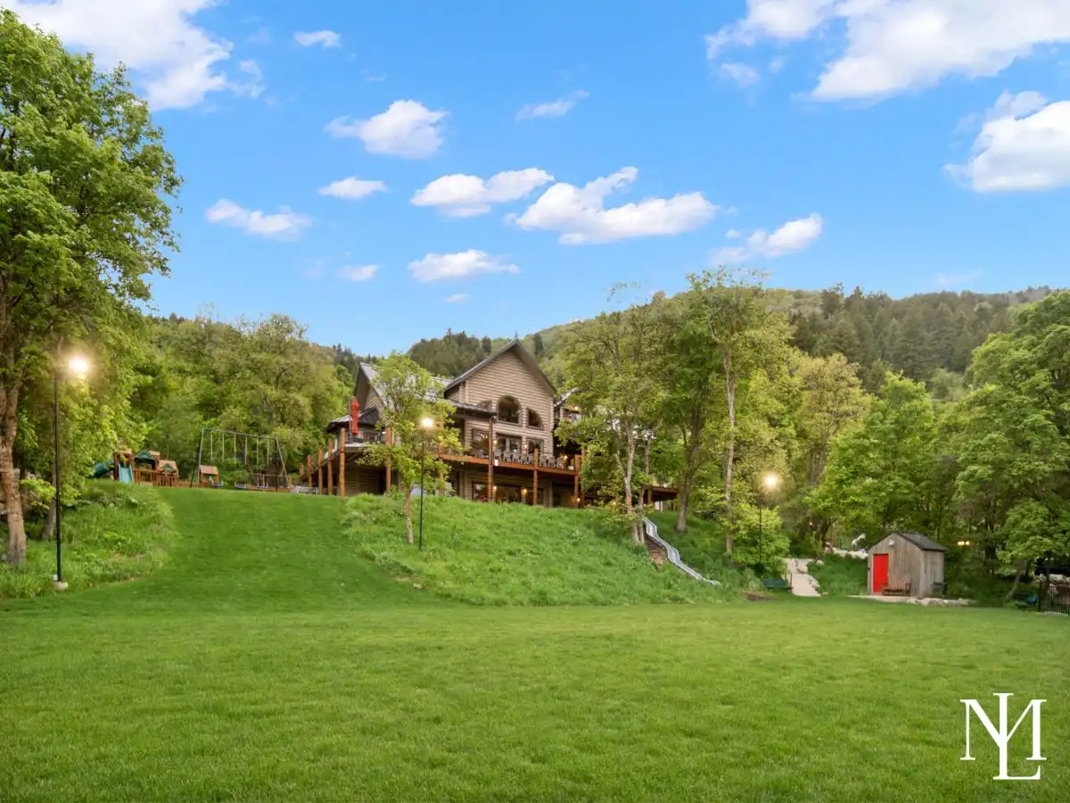 Expansive lawn and hillside setting with a luxury log cabin, playground, and outdoor recreation areas.