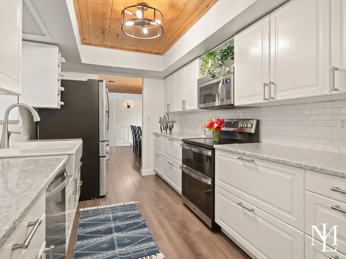 Remodeled kitchen with white cabinetry, granite countertops, stainless steel appliances, and wood ceiling detail.