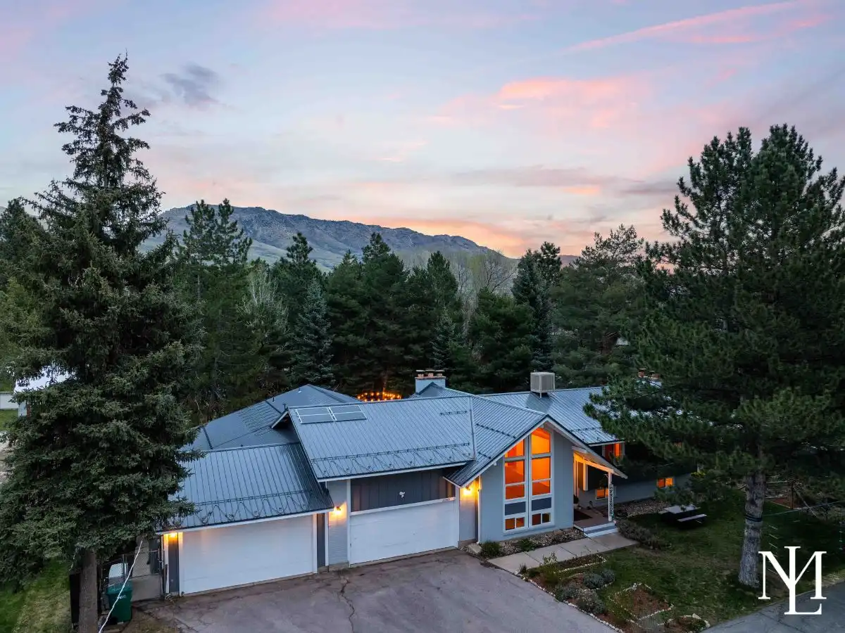 Twilight aerial of remodeled mountain home in Eden, Utah surrounded by mature pines with a metal roof and mountain backdrop.