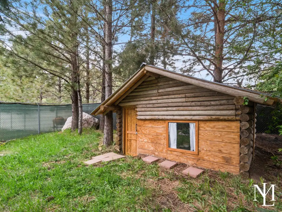 Rustic log playhouse or storage shed tucked beneath mature trees in private backyard oasis.