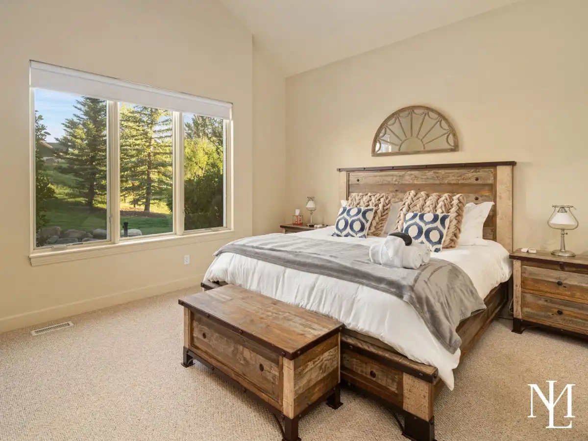 Primary bedroom in furnished Eden Utah home with rustic wood furniture, large window, and mountain retreat style