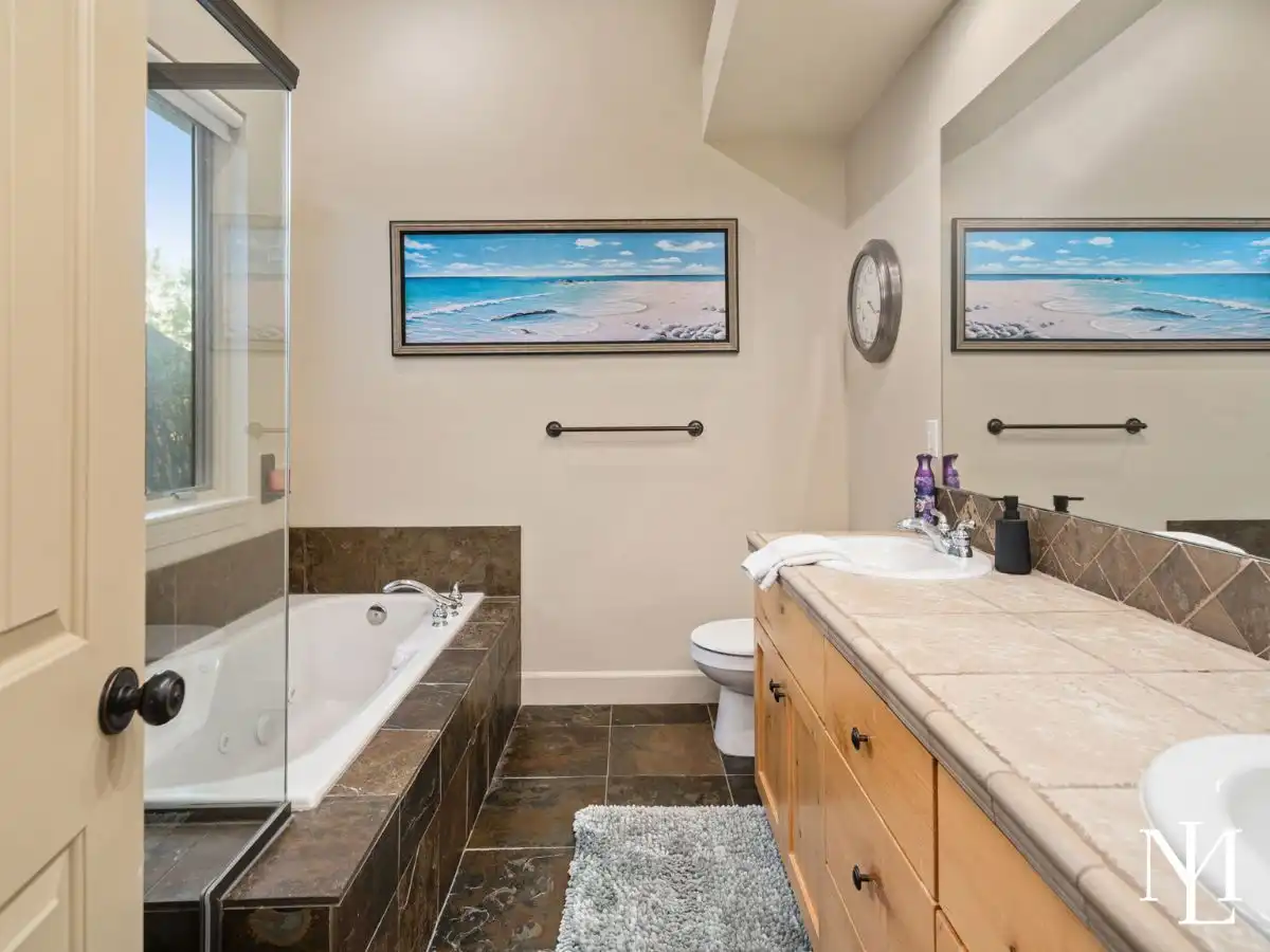 Primary bathroom in Eden mountain home with jetted tub, tile surround, wood vanity, and glass shower