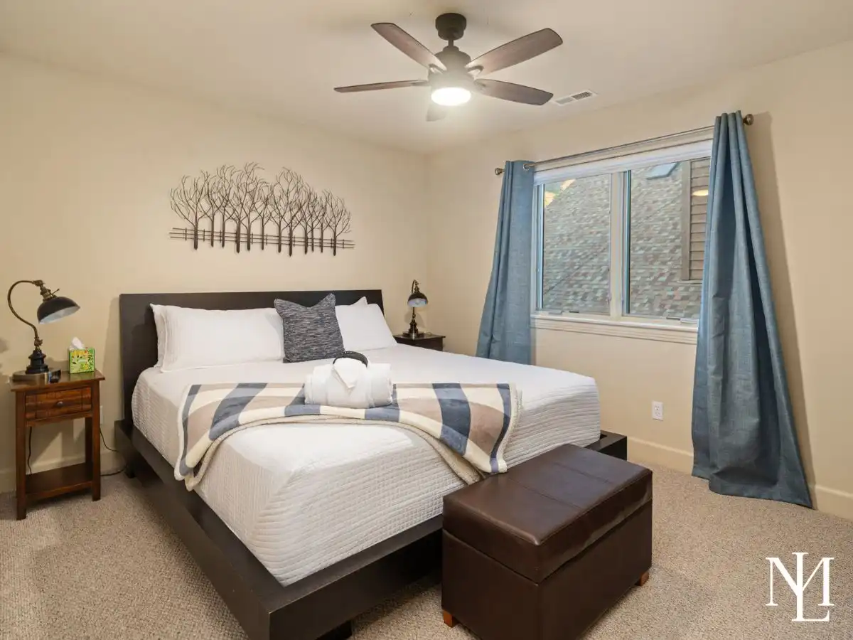 Furnished bedroom in Eden Utah vacation home with ceiling fan, blue curtains, and turnkey mountain lodging setup