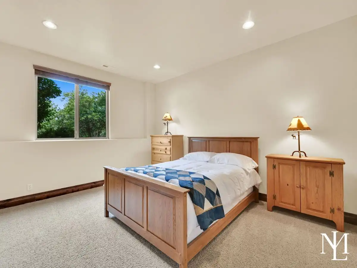 Lower-level bedroom in Eden Utah mountain home with wood bed frame, neutral carpet, recessed lighting, and window views