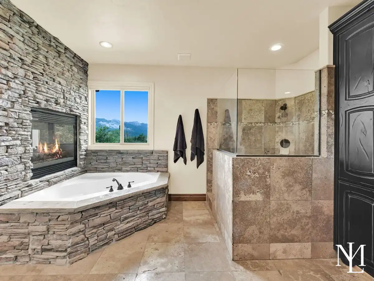 Primary bathroom in Eden mountain home with stone fireplace, soaking tub, glass shower, and mountain views