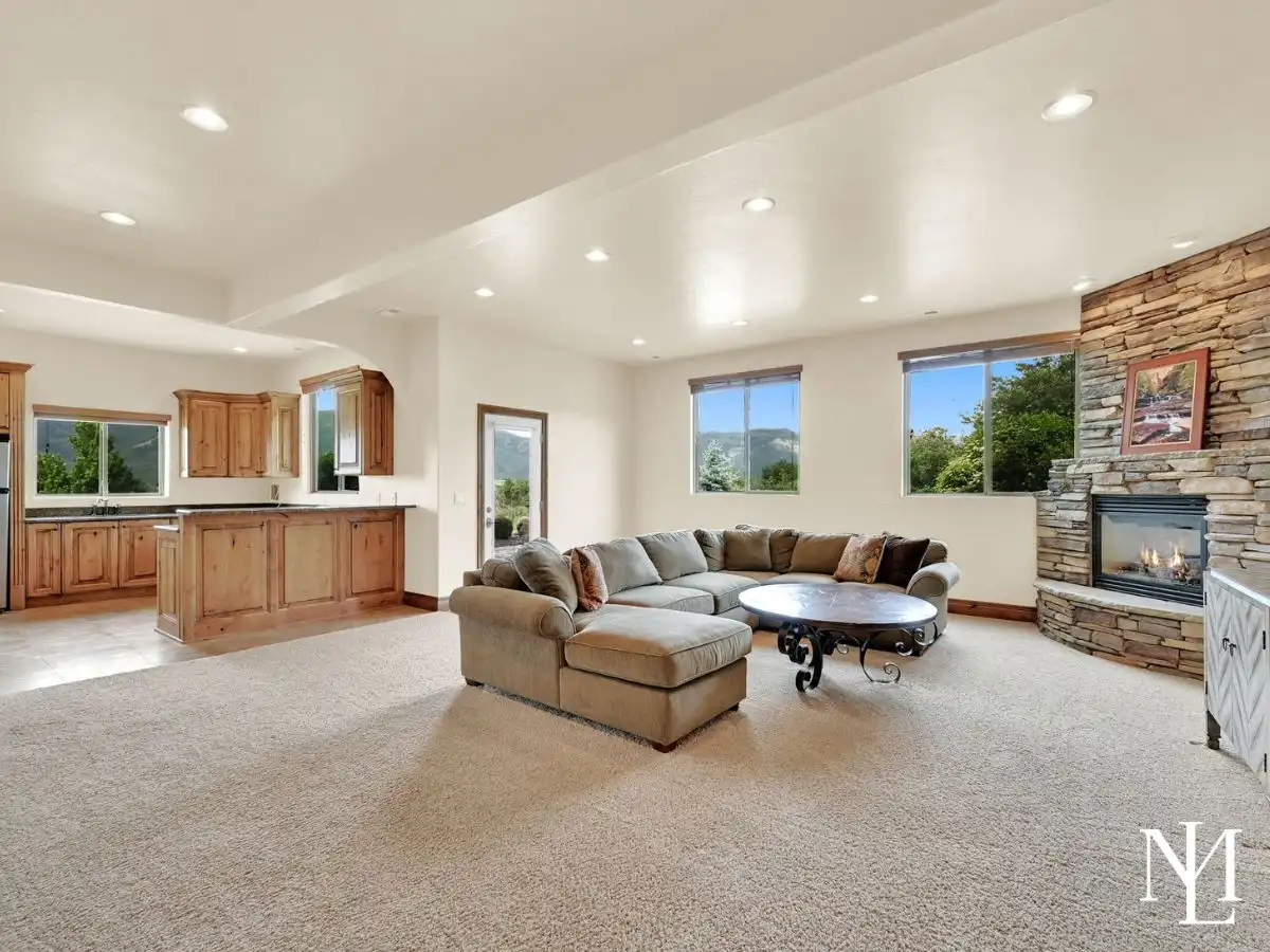 Lower-level living area in Eden Utah home with stone fireplace, guest kitchen, large windows, and mountain views