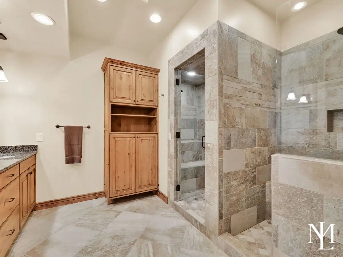 Spacious bathroom in Eden Utah home with tile walk-in shower, soaking tub, custom cabinetry, and natural stone finishes