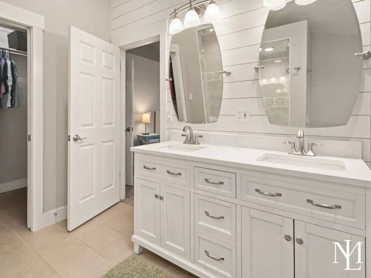 Primary bathroom vanity with double sinks, white cabinetry, shiplap accent wall, and modern mirrors.