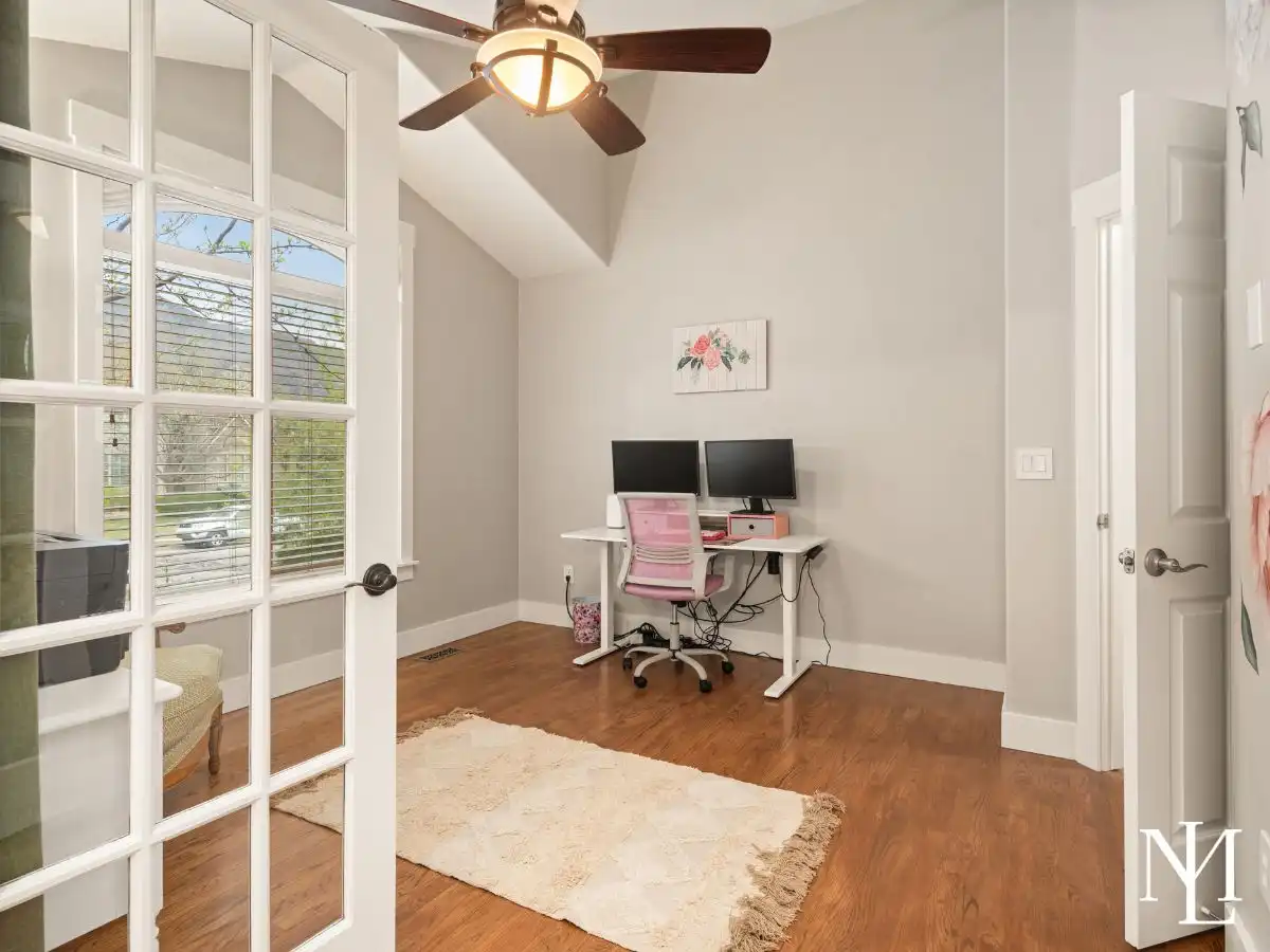 Home office with glass French doors, vaulted ceiling, hardwood floors, and front-facing window in Pleasant View home.