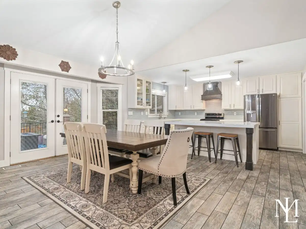 Dining area and remodeled kitchen with white cabinetry, large island, tile flooring, and French doors to deck.