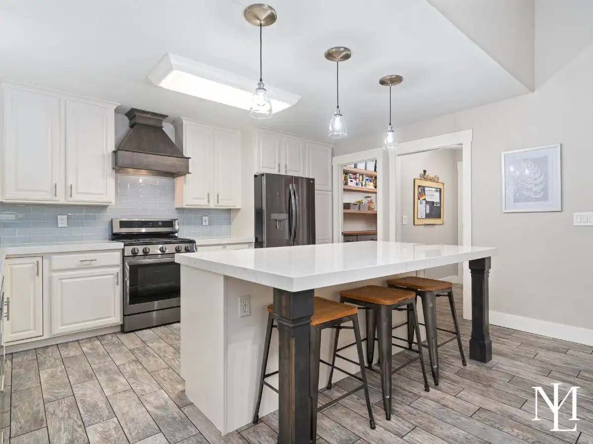 Updated kitchen with oversized island, quartz countertops, white cabinets, stainless steel appliances, and pendant lighting.