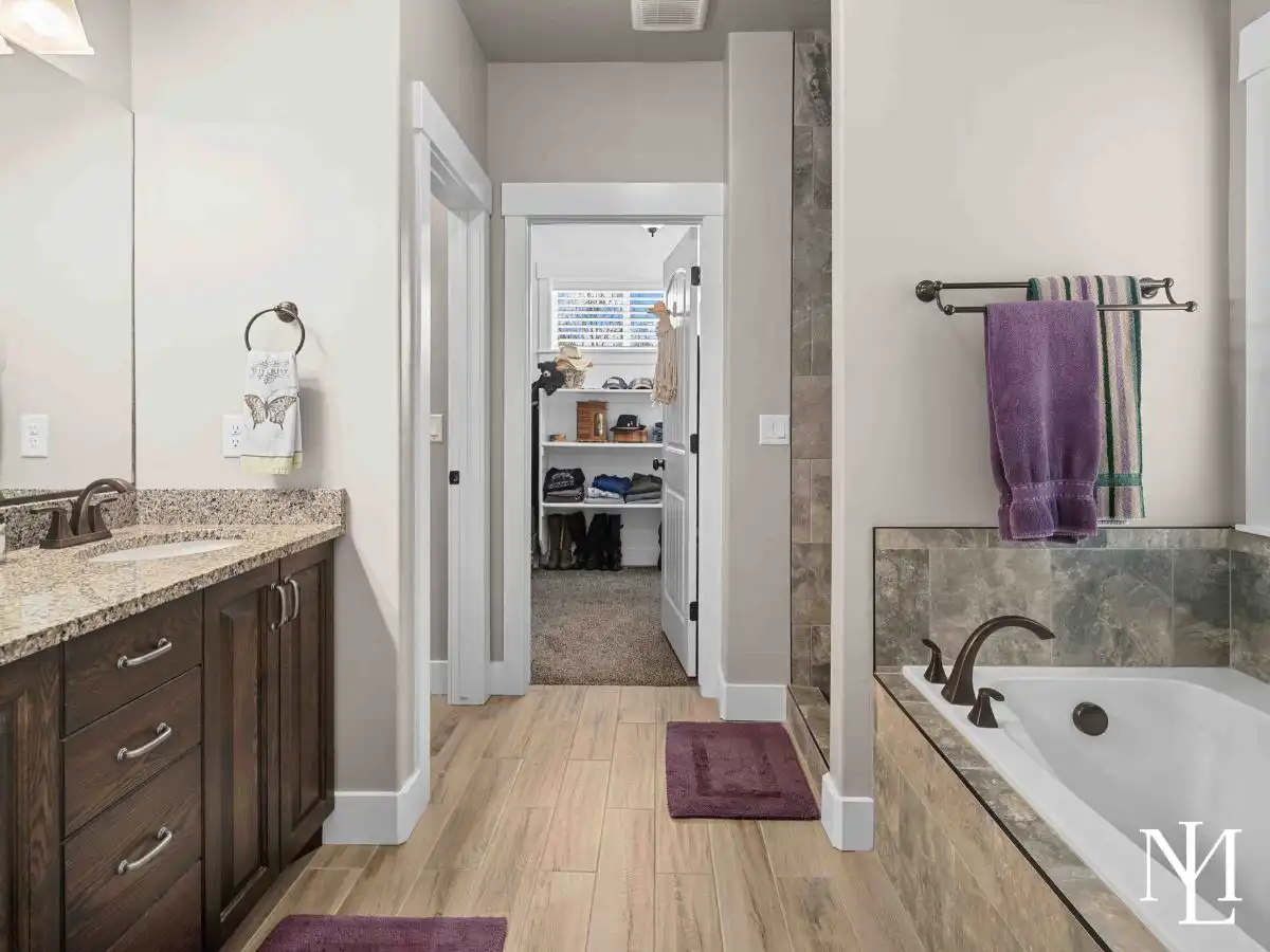 Primary bathroom with granite vanity, soaking tub, tile flooring, and walk-in closet access.