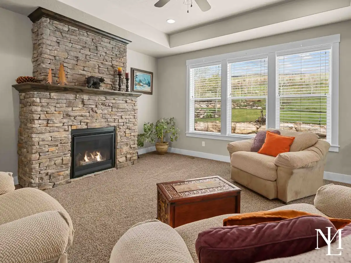 Living room with floor-to-ceiling stone fireplace, large windows, and views of the landscaped backyard.
