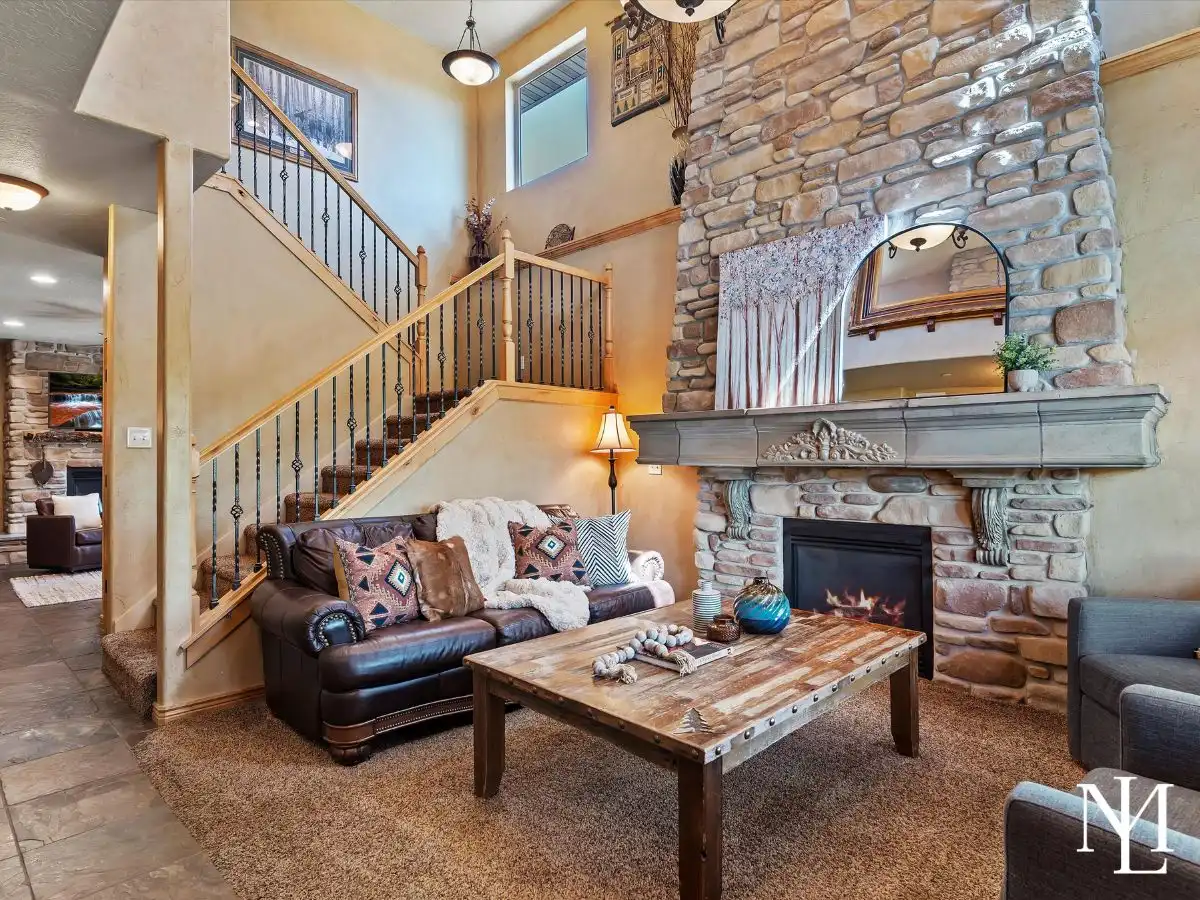 Warm lodge-style living room with soaring stone fireplace, staircase, and mountain home finishes in Eden, Utah.