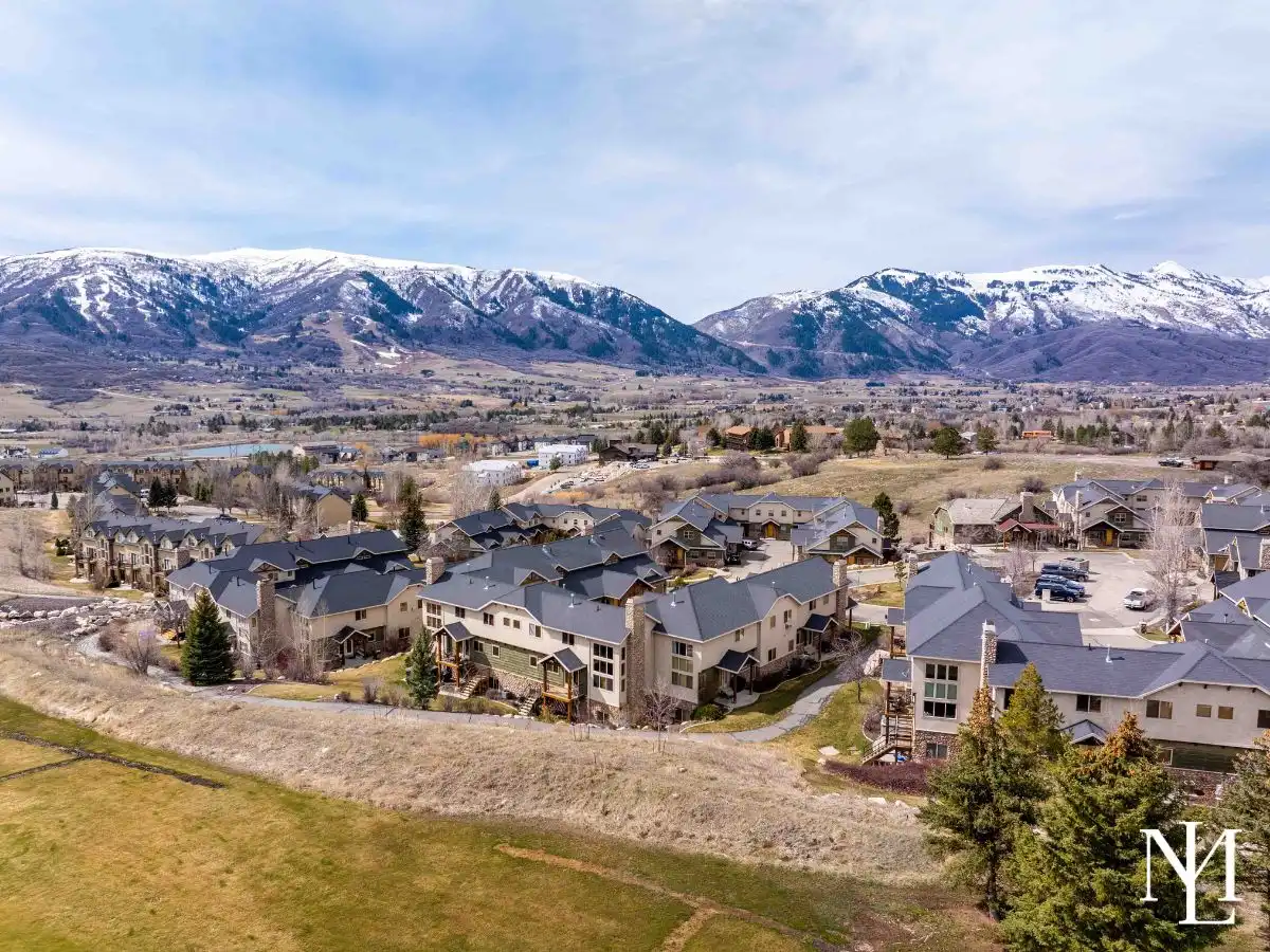 Drone view of The Cascades townhomes in Eden, Utah with Ogden Valley neighborhood rooftops and snowy mountain backdrop.