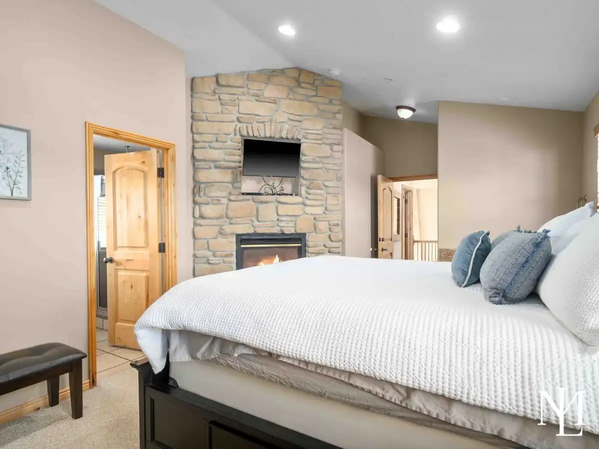 Bedroom featuring a stone fireplace and mounted TV with ensuite access in The Cascades townhome in Eden, Utah