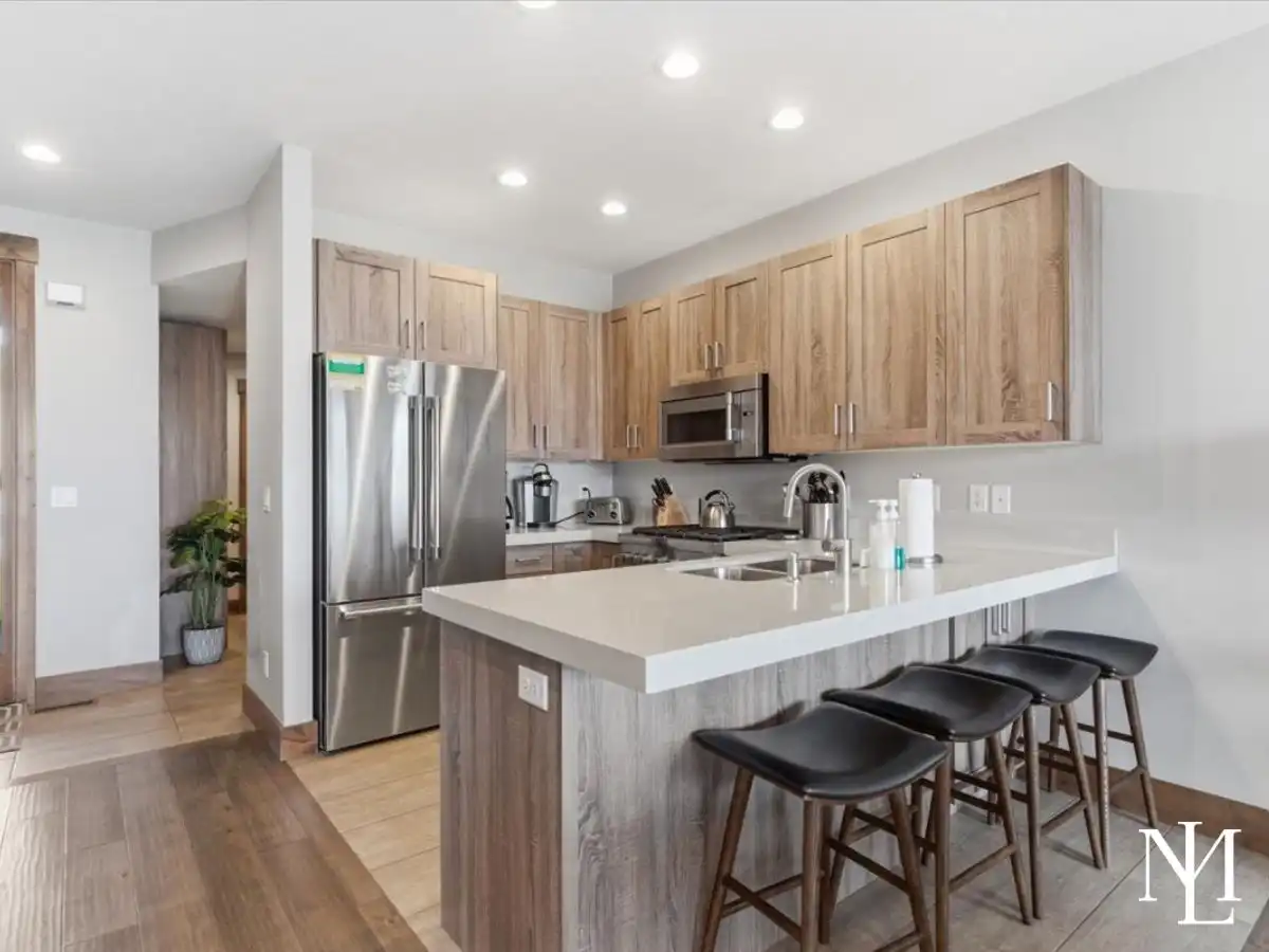 Modern kitchen with wood cabinetry, quartz island, stainless appliances, and bar seating.