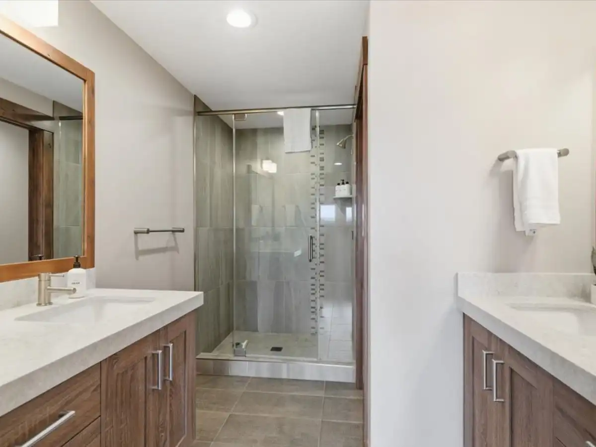 Bathroom with dual vanities, wood cabinetry, and glass walk-in shower.