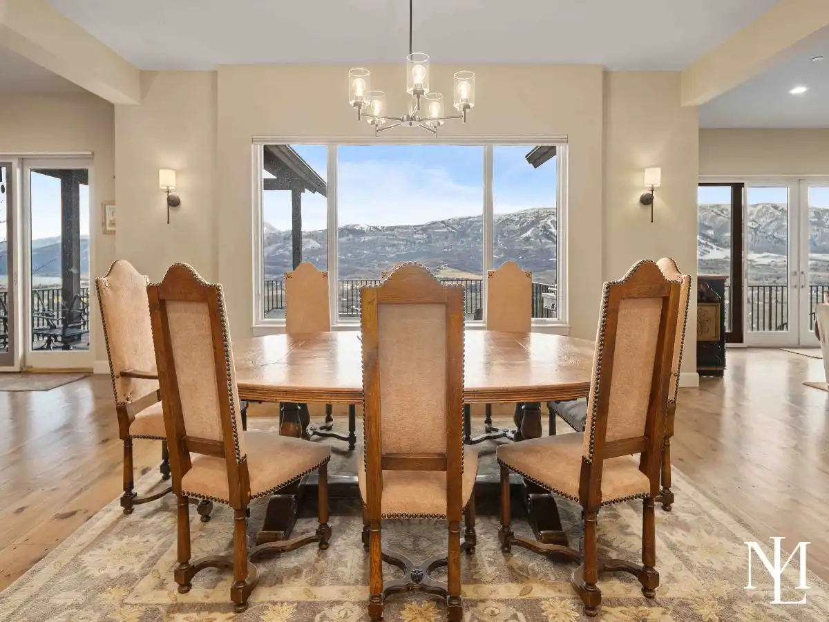 Elegant dining area with round table and upholstered chairs near windows with balcony and mountain views