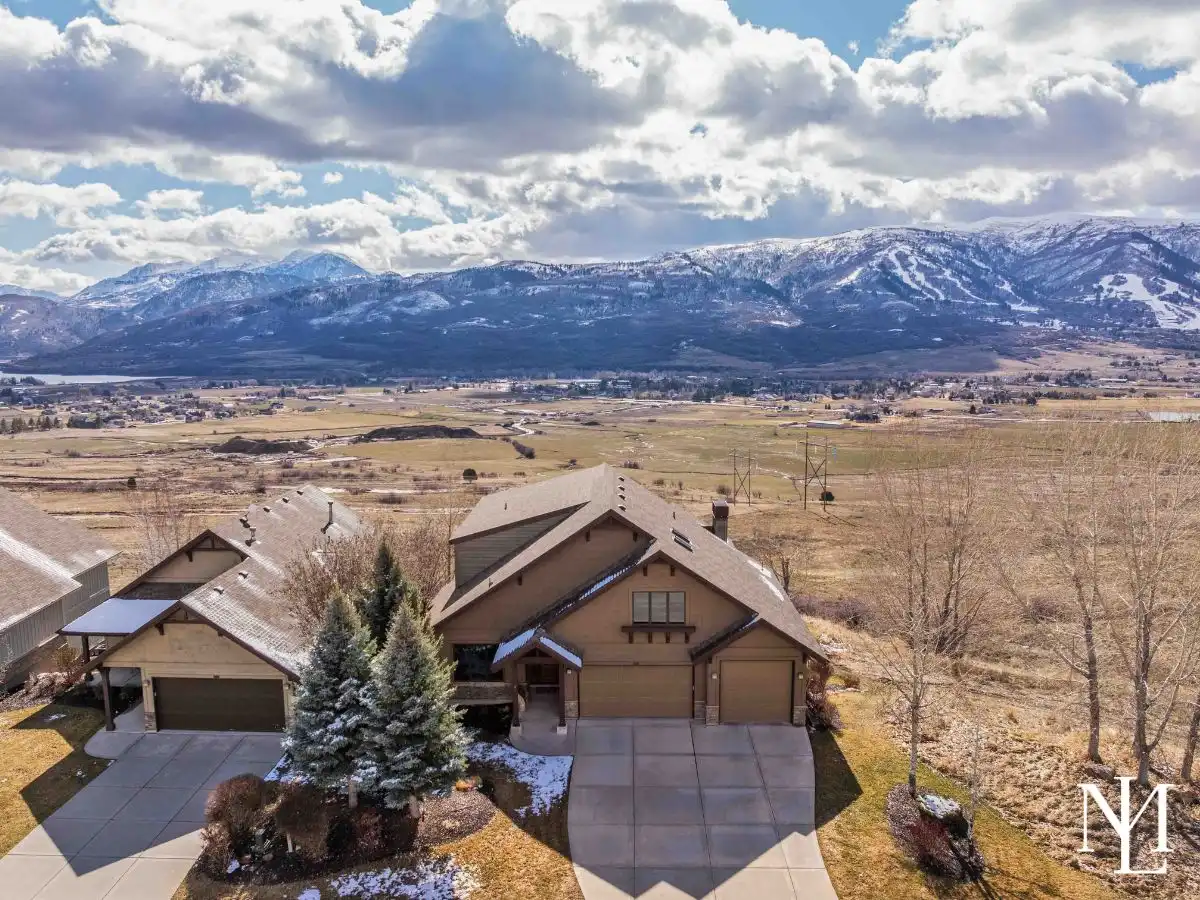 Aerial view of mountain homes in winter with ochre lands, mountain ranges, and Pineview Reservoir behind them
